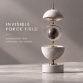 HOMZURE orbital balance sculpture with pale veined upper and lower half-spheres framing a dark sphere and gold-tone ring on a round base