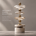 Front view of HOMZURE vertical orbit sculpture showing transparent discs and gold-tone spheres