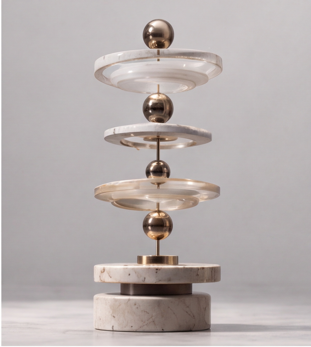 Close-up of the stacked clear discs, pale veined rims and gold-tone spheres of the HOMZURE sculpture