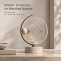 HOMZURE sculpture with clear concentric rings, pale speckled sphere, gold-tone curved arc and round base on a plain background